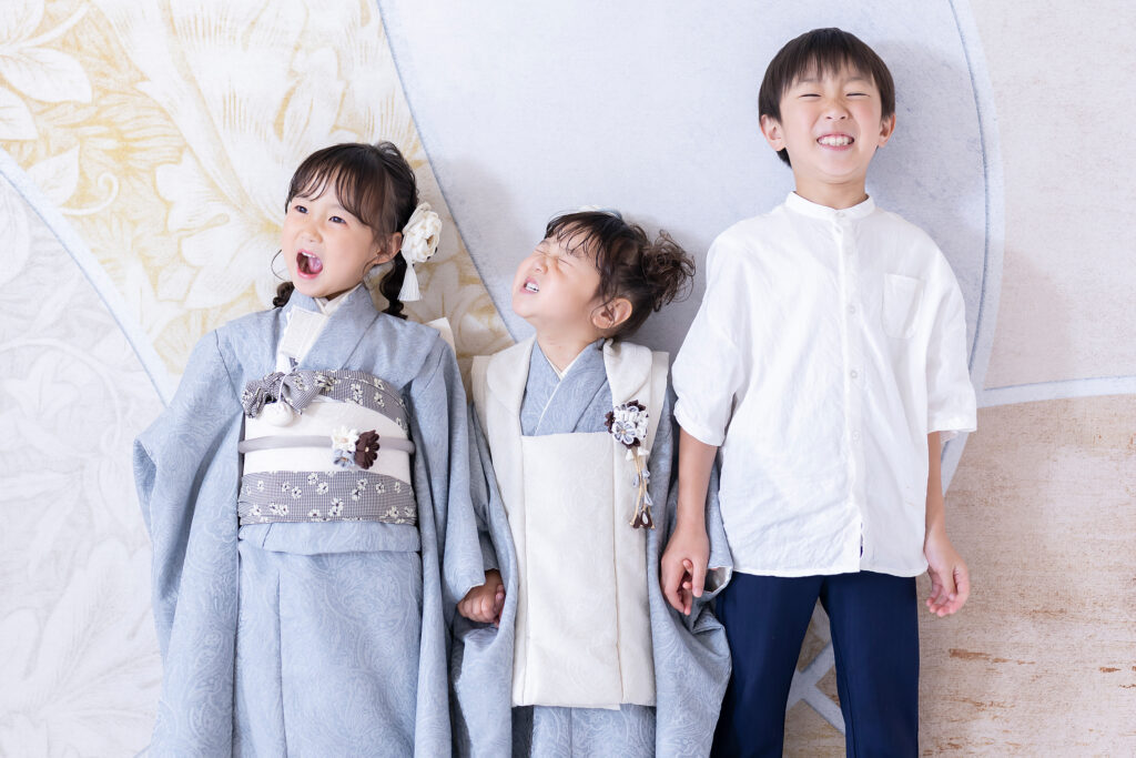 七五三の7歳と3歳の姉妹とお兄ちゃん、水色のモダンな着物でスタジオ撮影した3人の自然な笑顔の写真