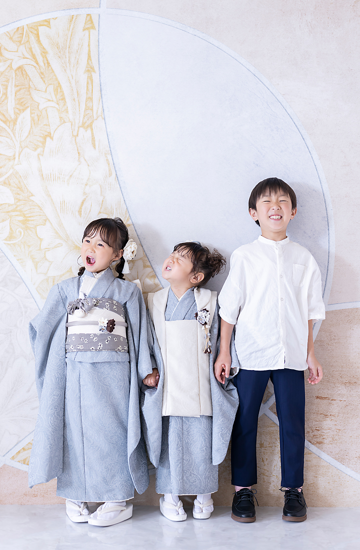 七五三の7歳と3歳の姉妹とお兄ちゃん、水色のモダンな着物でスタジオ撮影した3人の自然な笑顔の写真
