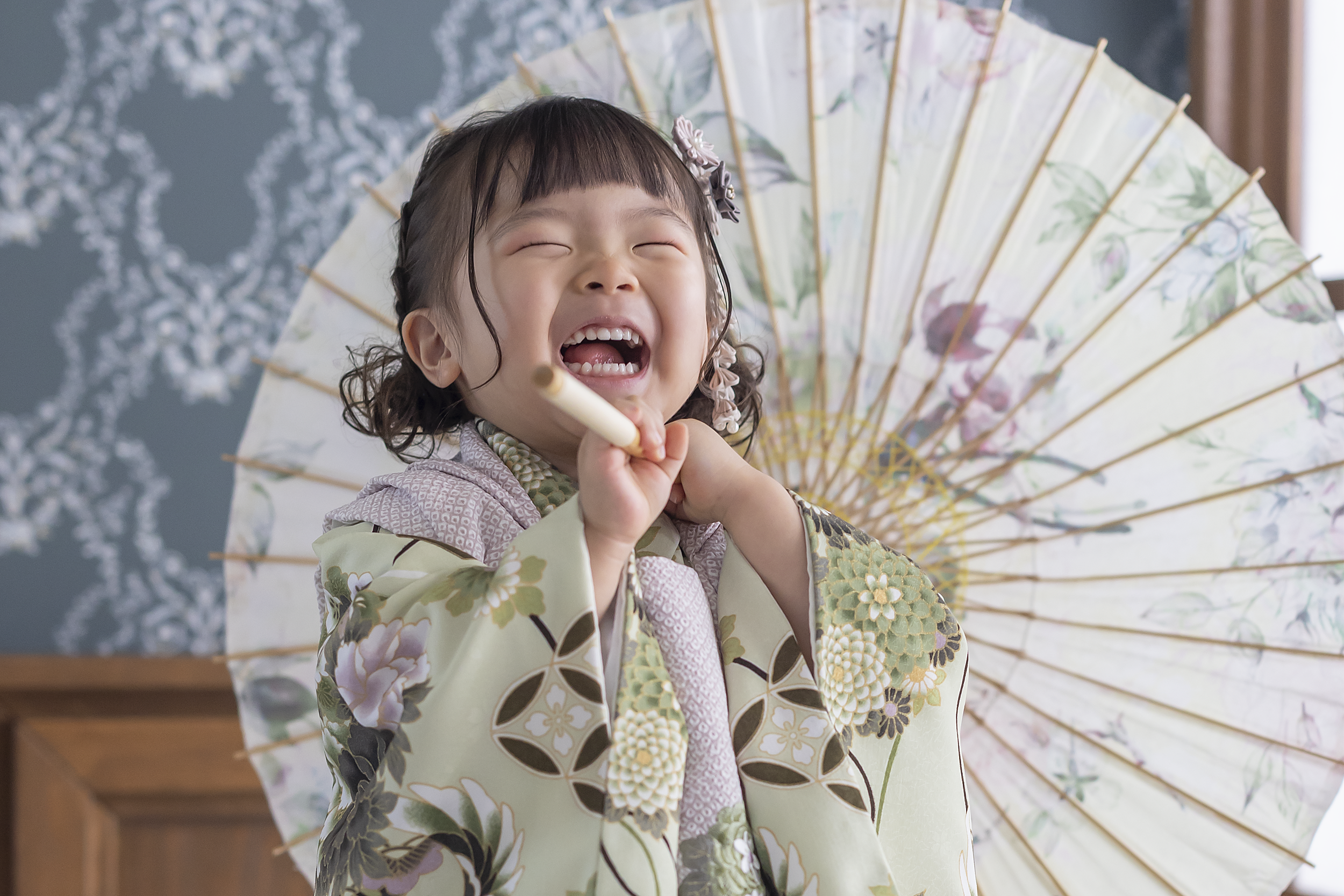 七五三の三歳の女の子が色鮮やかな着物を着て番傘を持ち、笑顔で立っている写真