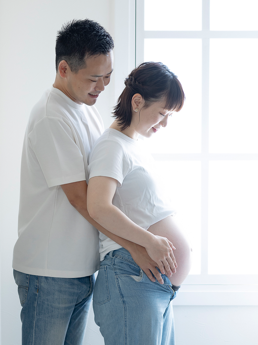 自然光の中でお腹を見つめる幸せそうな夫婦のマタニティフォト